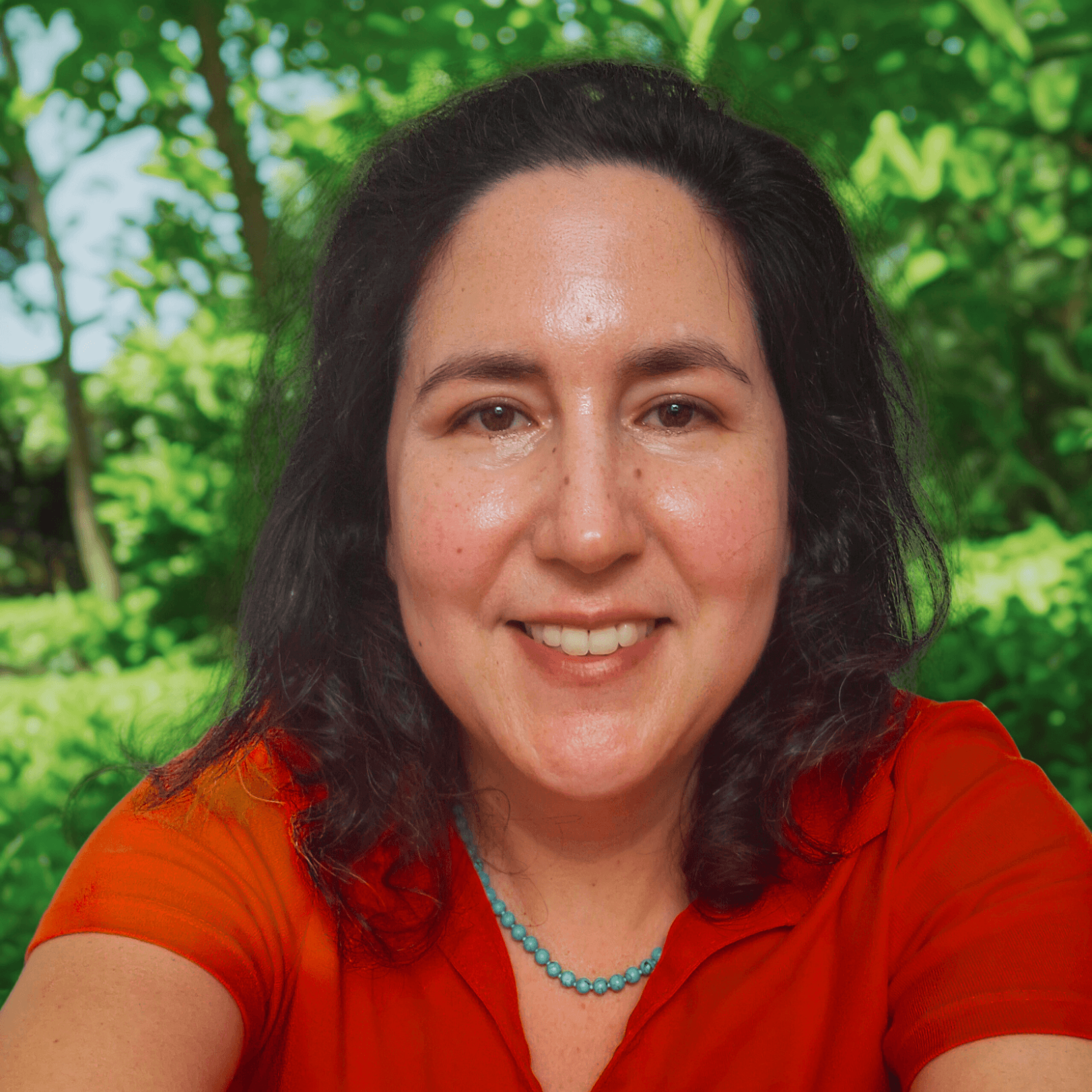 Vrouw met een glimlach in een groene omgeving, gekleed in een oranje shirt.