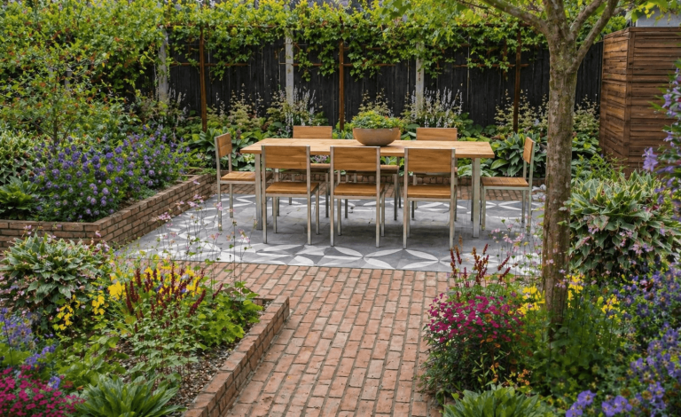 Een tuin met een houten eettafel en stoelen, omringd door bloeiende planten.